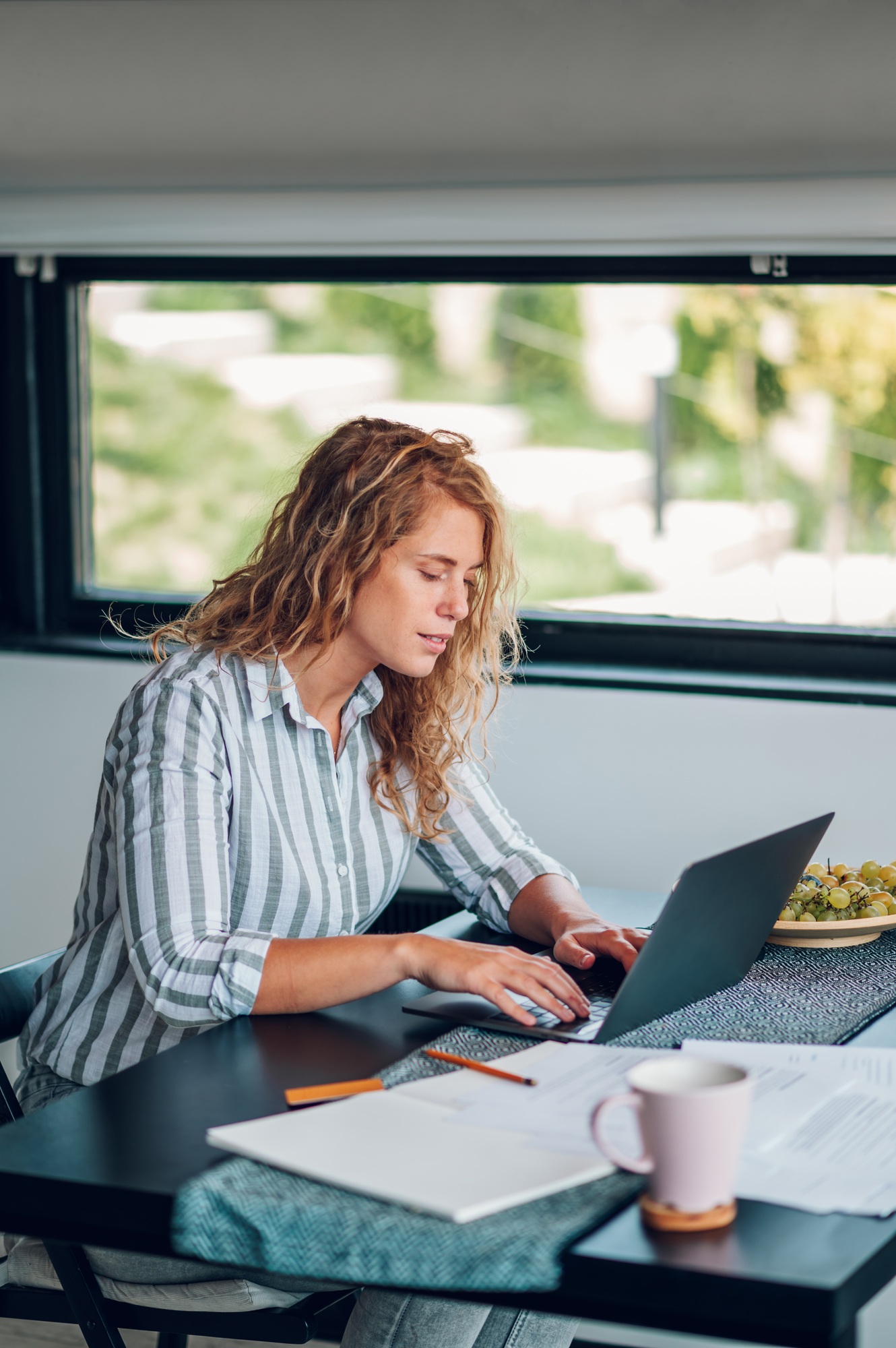 Young woman working in the kitchen at home with laptop and papers on desk